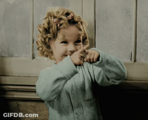 A Little Girl With Curly Hair Is Pointing Her Finger At Something GIF