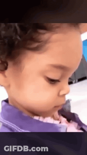 A Little Girl With Curly Hair Is Wearing A Purple Jacket And Looking At The Camera . GIF