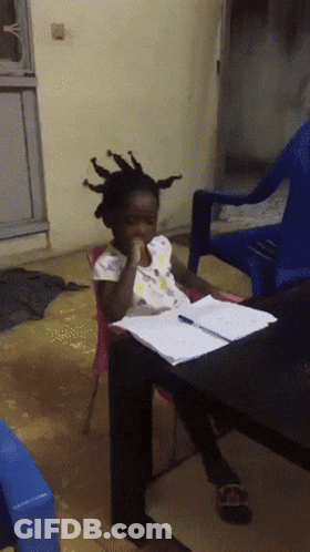 A Little Girl With Dreadlocks Sits At A Table With A Pen In Her Hand GIF
