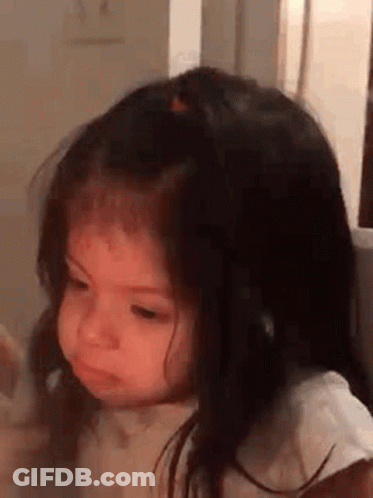 A Little Girl With Long Hair Is Making A Funny Face While Sitting In A Chair . GIF