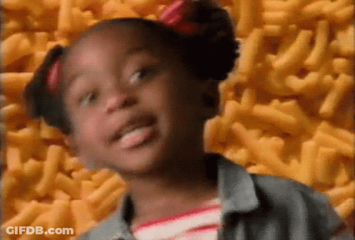 A Little Girl With Pigtails Is Standing In Front Of A Pile Of Macaroni And Cheese . GIF