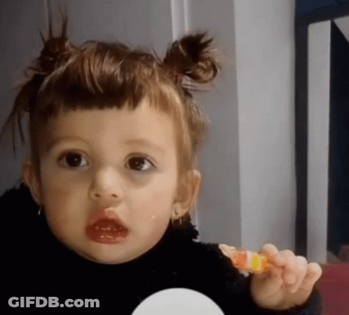 A Little Girl With Pigtails On Her Hair Is Holding A Lollipop In Her Hand GIF