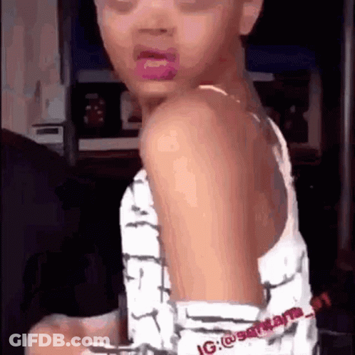A Little Girl With Pink Lipstick On Her Lips Is Sitting In A Chair And Looking At The Camera . GIF