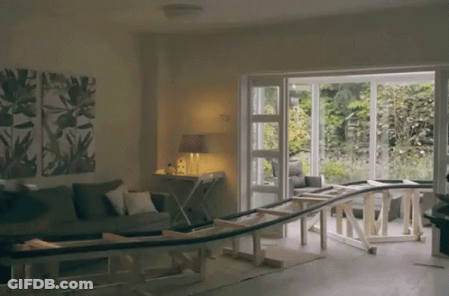 A Living Room With A Couch And A Table With A Wooden Railing Going Through It GIF