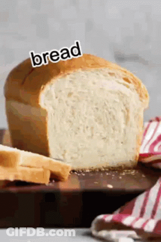 A Loaf Of Bread Is Sitting On A Wooden Cutting Board With A Knife . GIF