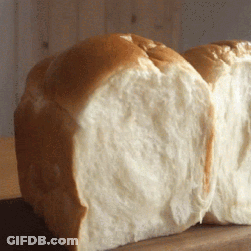 A Loaf Of Bread That Has Been Cut In Half Sits On A Wooden Table GIF