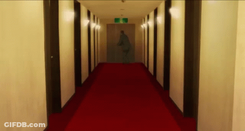 A Long Hallway With A Red Carpet And A Sign That Says Exit On It GIF