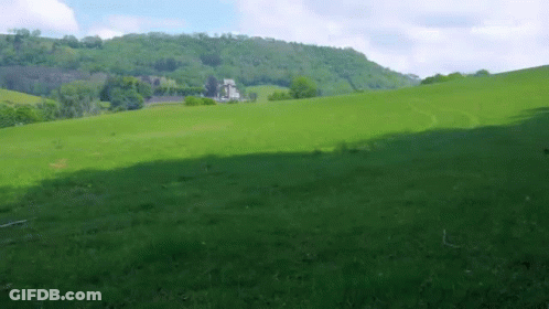 A Lush Green Field With A House On The Hill In The Background GIF