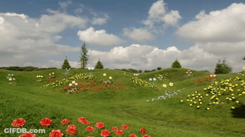 A Lush Green Field With Flowers And Trees In The Background GIF