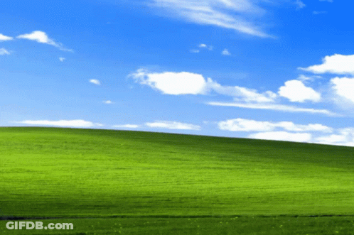 A Lush Green Hillside With A Blue Sky And White Clouds GIF