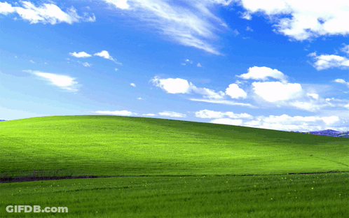 A Lush Green Hillside With A Blue Sky And White Clouds GIF