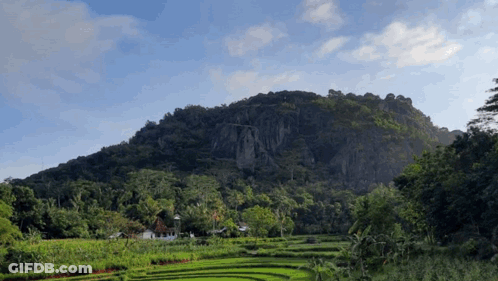 A Lush Green Hillside With A Few Houses In The Distance GIF