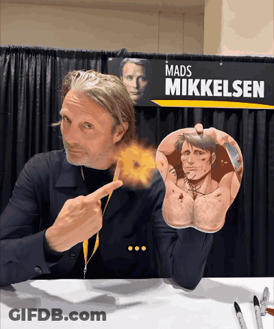 A Mads Mikkelsen Sign Hangs Above A Man 'S Arm GIF