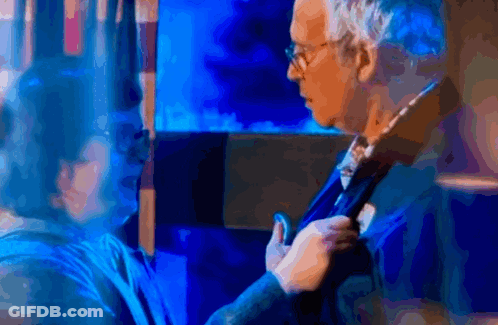 A Man Adjusts His Tie While A Woman Looks On In A Blurry Photo GIF