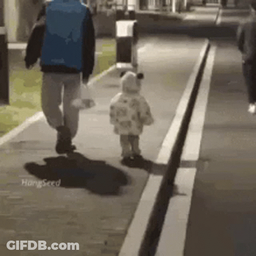 A Man And A Baby Are Walking Down A Sidewalk At Night . GIF