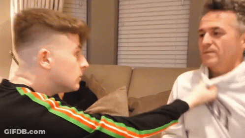 A Man And A Boy Are Sitting On A Couch And The Boy Is Holding The Man 'S Shirt . GIF