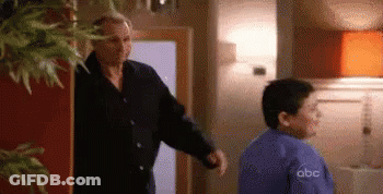 A Man And A Boy Are Standing In A Room . GIF