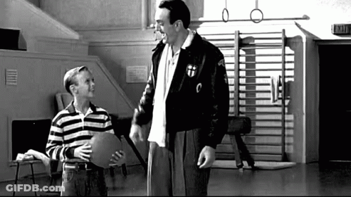 A Man And A Boy Are Standing Next To Each Other In A Gym . The Boy Is Holding A Piece Of Paper . GIF