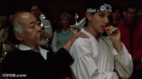 A Man And A Boy In Karate Uniforms Are Standing Next To Each Other In A Crowd GIF