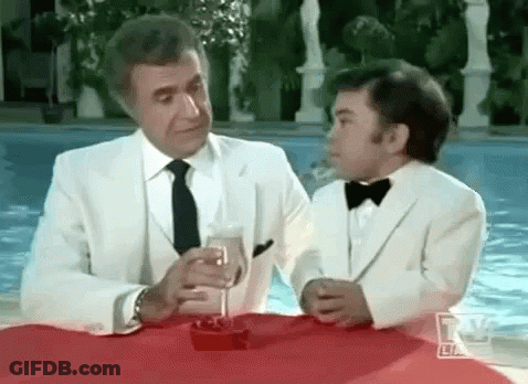 A Man And A Boy In Tuxedos Are Sitting At A Table With A Glass Of Champagne . GIF