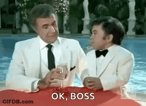 A Man And A Boy In Tuxedos Are Sitting At A Table With A Glass Of Wine And Talking . GIF