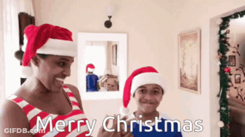 A Man And A Boy Wearing Santa Hats Say Merry Christmas In A Living Room GIF