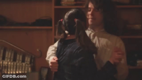 A Man And A Girl Are Hugging In Front Of A Bookshelf GIF