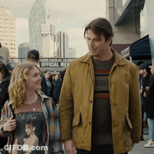 A Man And A Girl Are Standing Next To Each Other In Front Of A Sign That Says Official Merch GIF