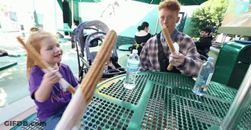 A Man And A Little Girl Are Eating Churros At A Table With A Bottle Of Aquafina Water On It GIF