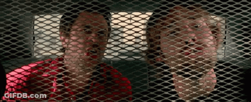 A Man And A Woman Are Behind A Mesh Fence GIF