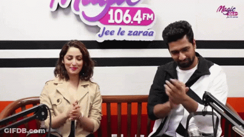 A Man And A Woman Are Clapping In Front Of A Sign That Says 106.4 Fm Jee Le Zaraa GIF