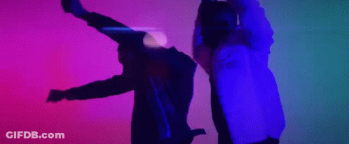 A Man And A Woman Are Dancing In A Dark Room With A Purple And Blue Light Behind Them . GIF