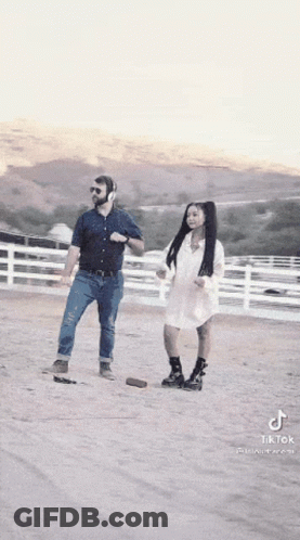 A Man And A Woman Are Dancing In A Dirt Field While Wearing Headphones . GIF