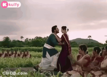 A Man And A Woman Are Dancing In A Field With A Group Of People Watching . GIF