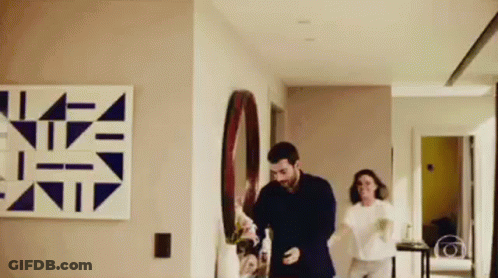 A Man And A Woman Are Dancing In A Hallway In A Living Room . GIF