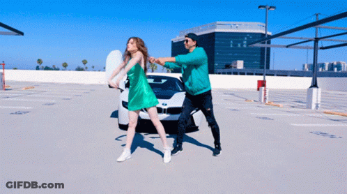 A Man And A Woman Are Dancing In A Parking Lot GIF