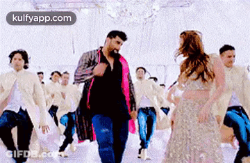 A Man And A Woman Are Dancing In A Room With A Group Of People . GIF