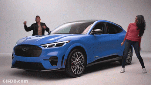 A Man And A Woman Are Dancing In Front Of A Blue Ford Mustang GIF