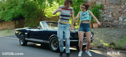 A Man And A Woman Are Dancing In Front Of A Blue Mustang Convertible . GIF