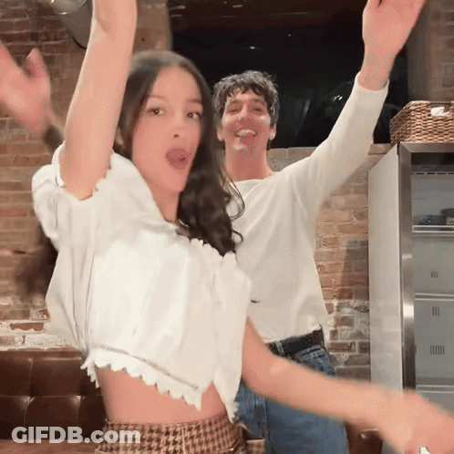 A Man And A Woman Are Dancing In Front Of A Brick Wall GIF