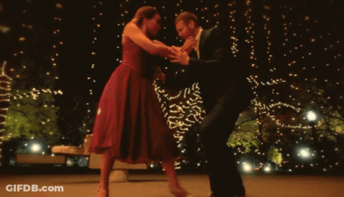A Man And A Woman Are Dancing In Front Of A Christmas Tree GIF
