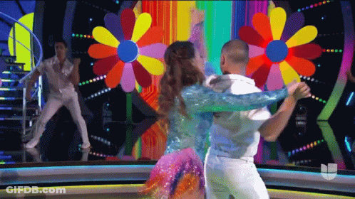 A Man And A Woman Are Dancing In Front Of A Colorful Flower Background GIF