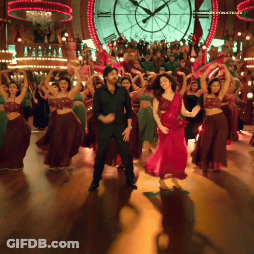 A Man And A Woman Are Dancing In Front Of A Large Clock That Says Mightymatelu GIF