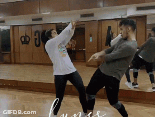 A Man And A Woman Are Dancing In Front Of A Mirror With A Crown On The Wall Behind Them GIF