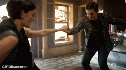 A Man And A Woman Are Dancing In Front Of A Sign That Says #Blindspot GIF