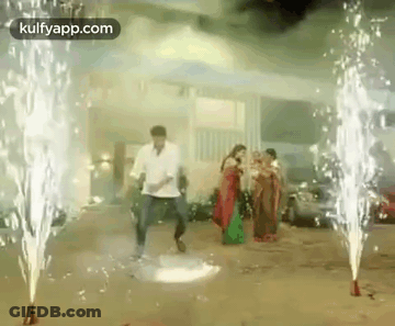 A Man And A Woman Are Dancing In Front Of Fireworks In A Parking Lot . GIF