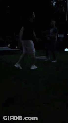 A Man And A Woman Are Dancing In The Dark On A Lush Green Field . GIF