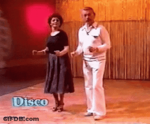 A Man And A Woman Are Dancing On A Dance Floor With A Disco Sign In The Background . GIF