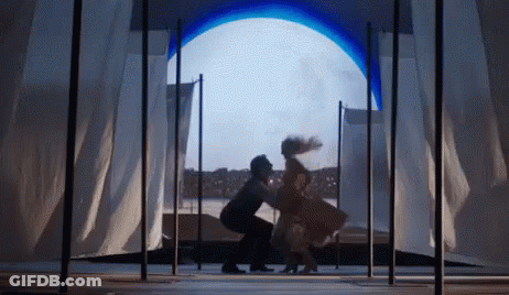 A Man And A Woman Are Dancing On A Stage In Front Of A Large Window . GIF