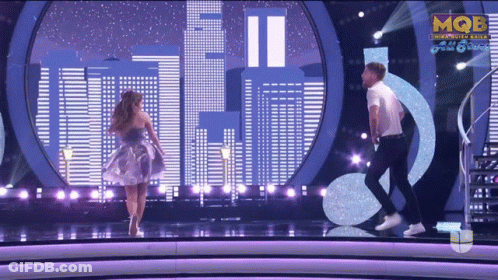 A Man And A Woman Are Dancing On A Stage With Mqbe On The Bottom Right GIF